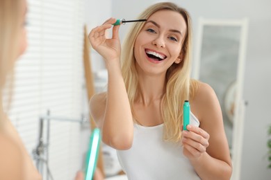 Photo of Beautiful woman applying mascara near mirror in bathroom