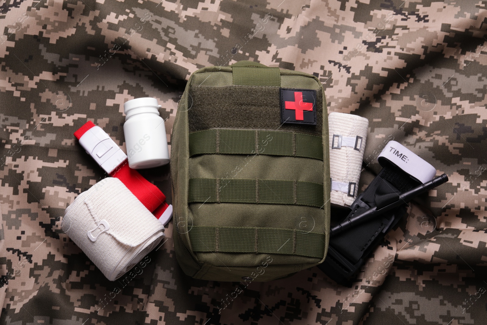 Photo of First aid kit with medical tourniquet, pills and bands on military fabric, flat lay