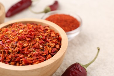 Photo of Chili pepper flakes and pods on light textured table, closeup. Space for text