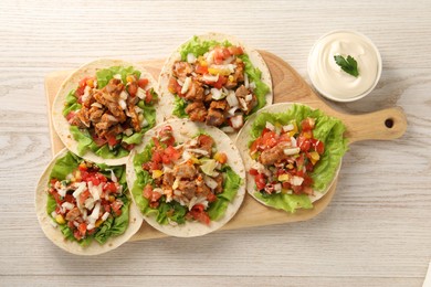 Photo of Delicious tacos with vegetables, meat and sauce on white wooden table, flat lay