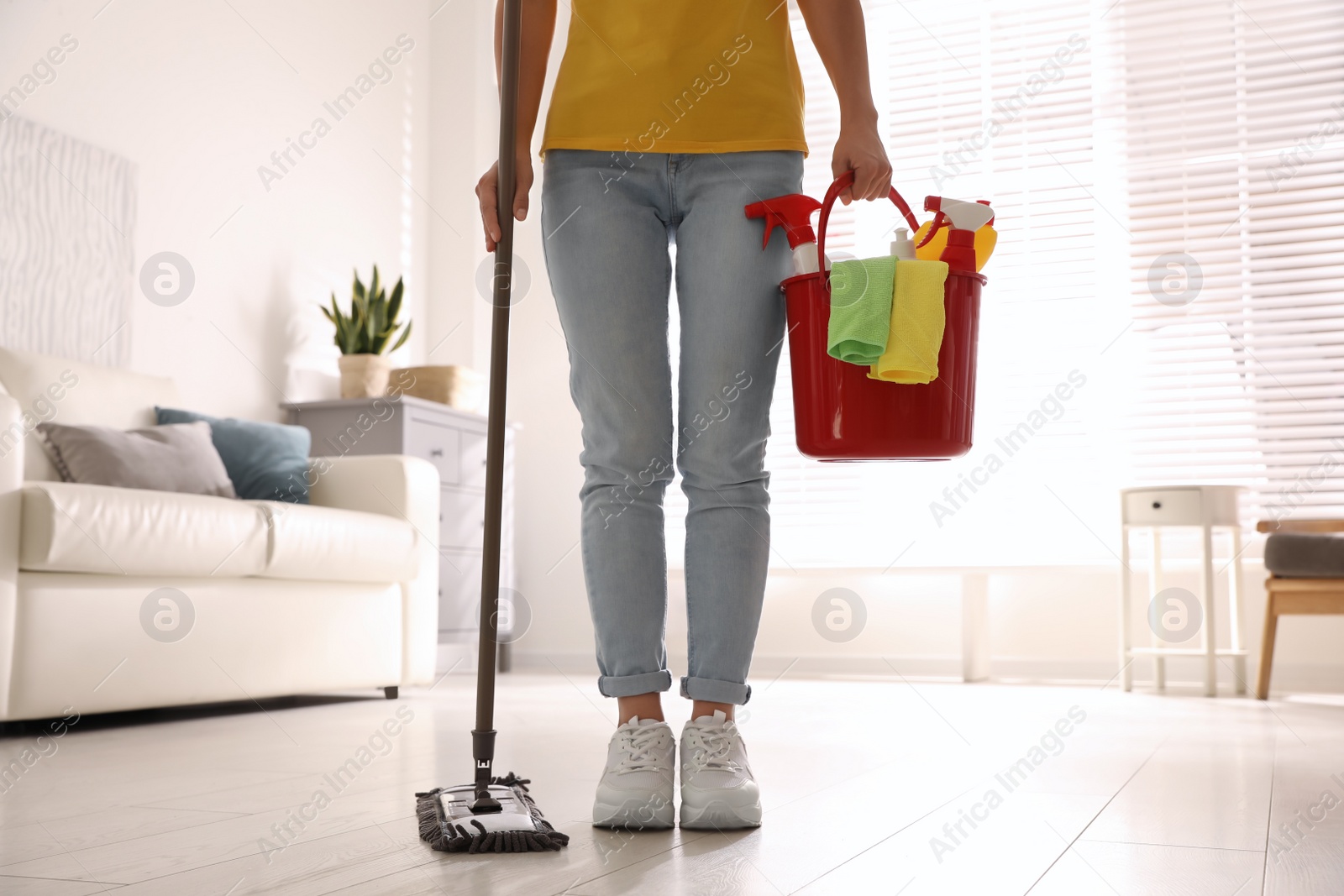 Photo of Woman with mop and bucket of cleaning supplies in room, closeup