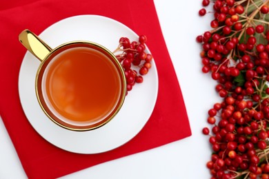 Cup of tea and fresh ripe viburnum berries on white table, flat lay