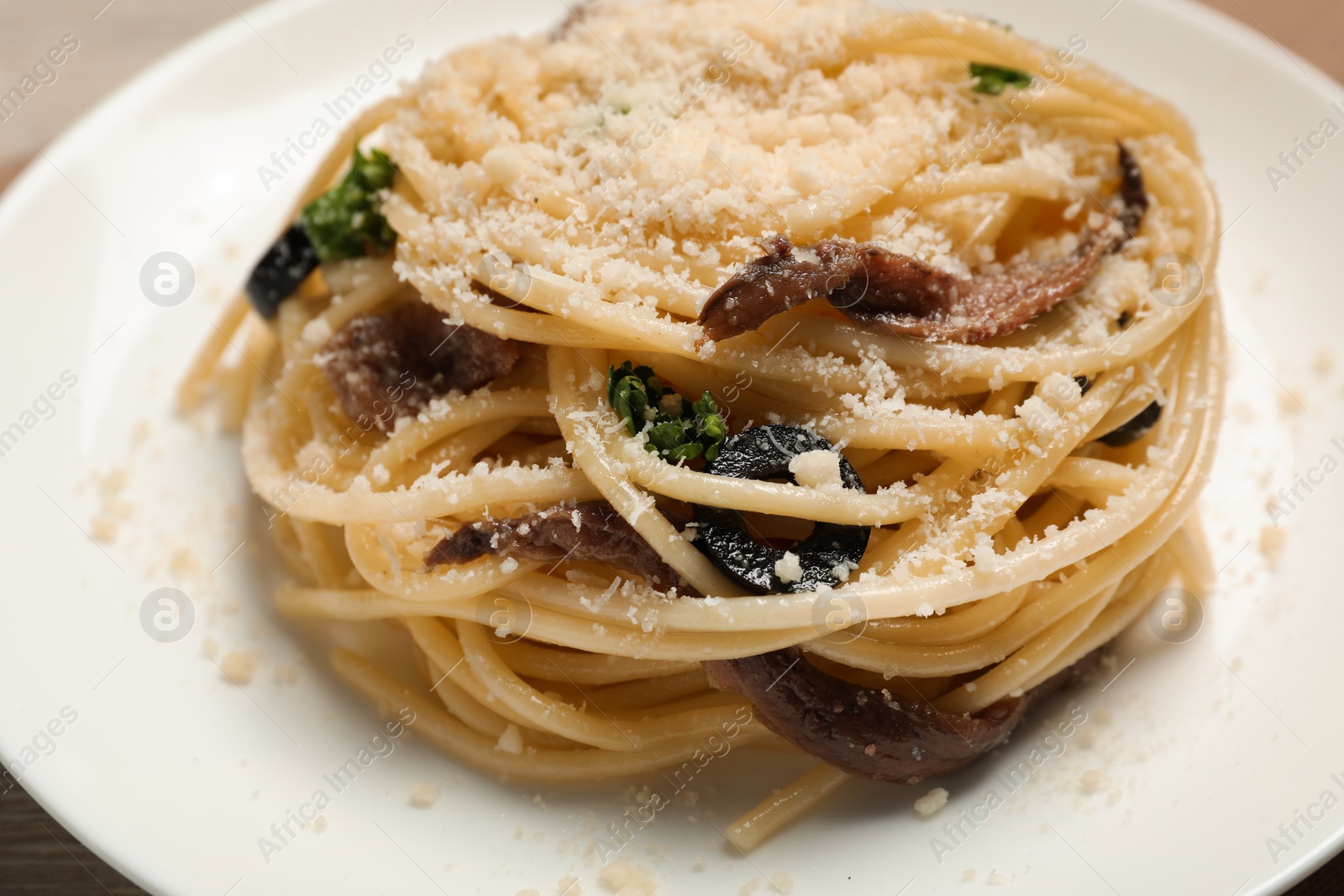 Photo of Delicious pasta with anchovies, olives and parmesan cheese served on table, closeup