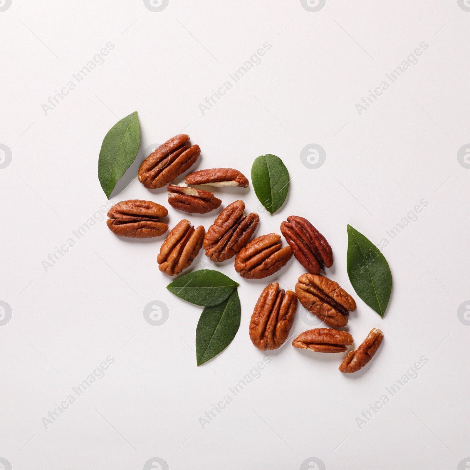 Photo of Delicious pecan nuts and green leaves on white background, flat lay