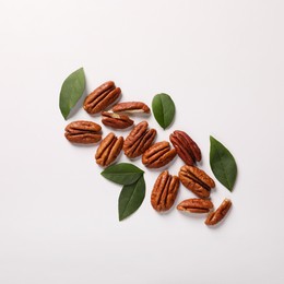 Delicious pecan nuts and green leaves on white background, flat lay