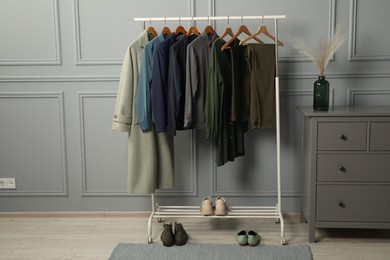 Photo of Rack with different stylish women`s clothes, shoes and chest of drawers near grey wall indoors