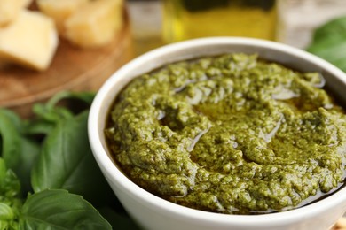 Photo of Tasty pesto sauce in bowl and basil on table, closeup