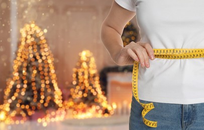 Image of Woman measuring waist with tape in room decorated for Christmas, closeup