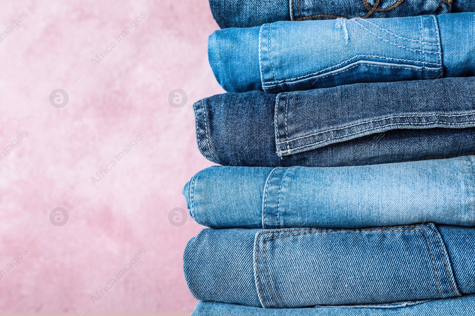 Photo of Stack of different jeans on pink background, closeup