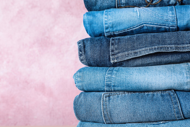 Stack of different jeans on pink background, closeup