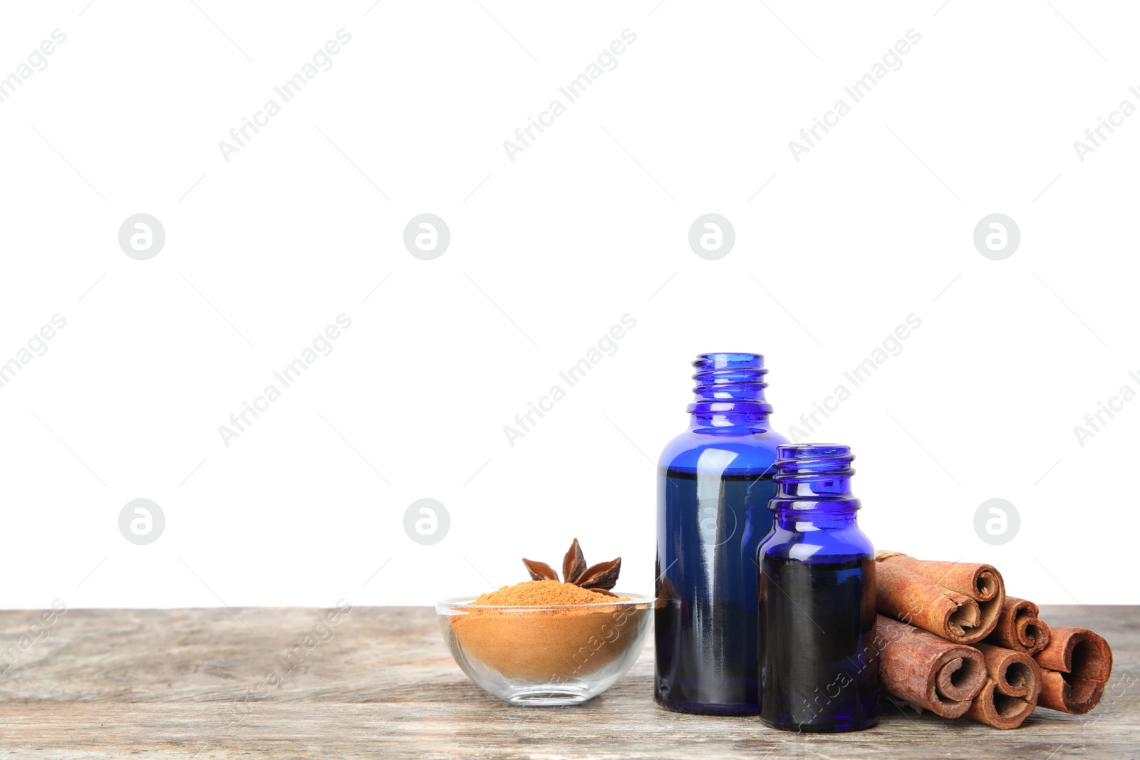 Photo of Bottles of essential oils, cinnamon sticks and powder on wooden table against white background. Space for text