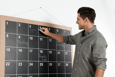 Handsome man writing with chalk on board calendar