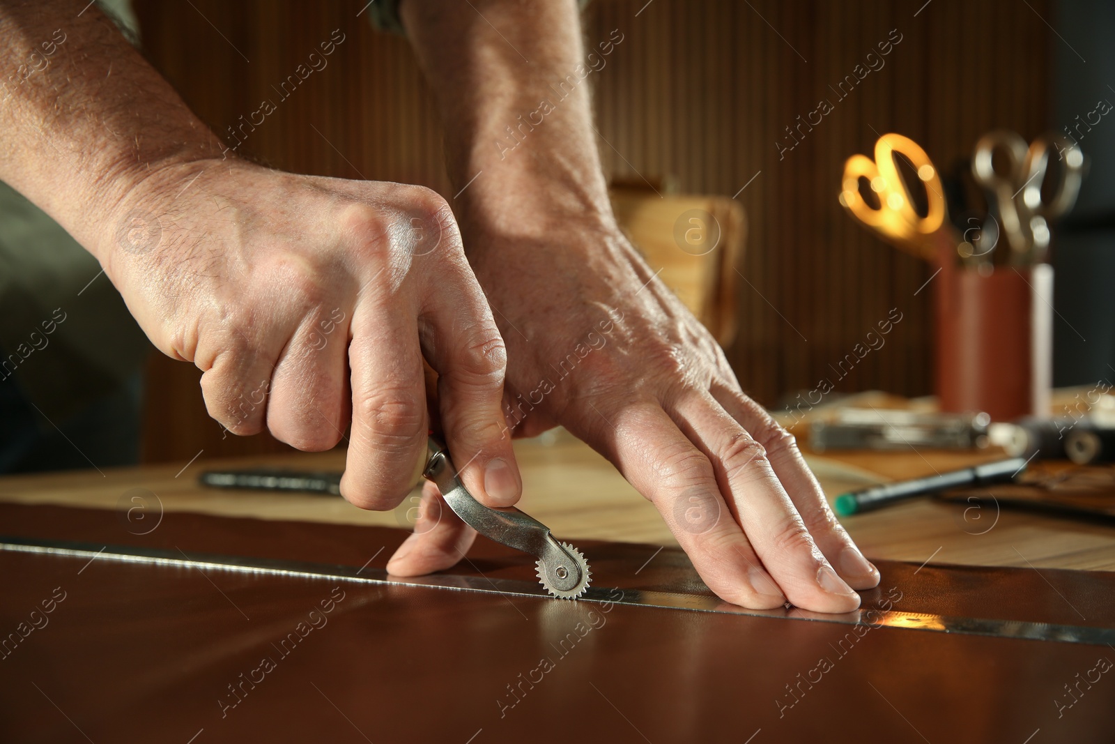 Photo of Man marking leather with roller in workshop, closeup