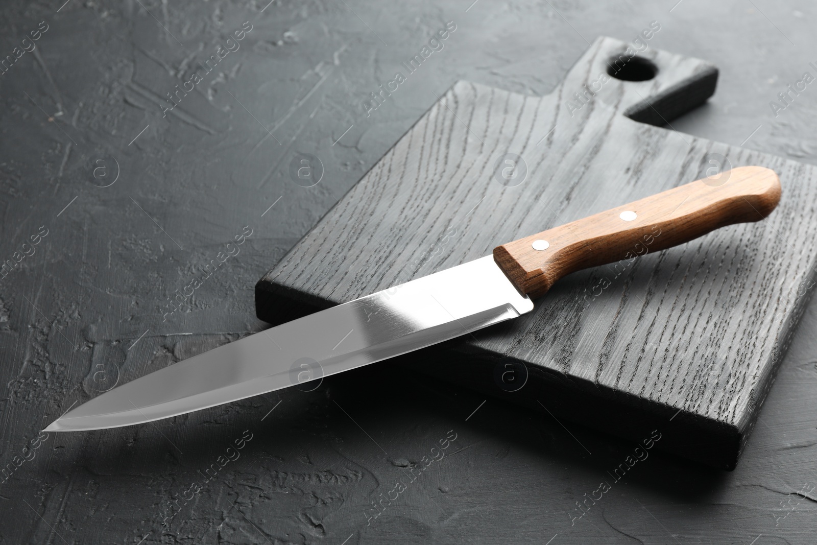 Photo of One sharp knife and board on dark textured table, closeup