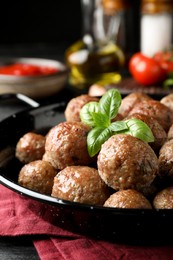 Photo of Tasty cooked meatballs with basil on black wooden table, closeup