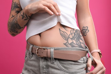 Photo of Woman with tattoos on body against pink background, closeup