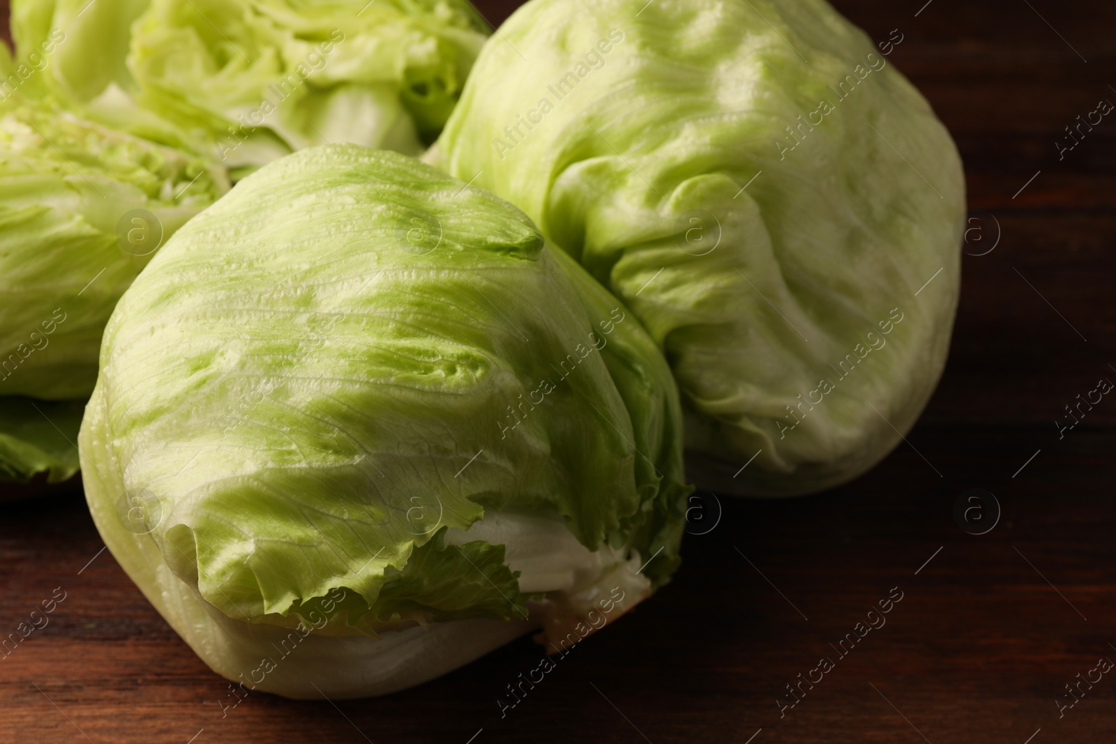 Photo of Fresh green whole and cut iceberg lettuce heads on wooden table, closeup