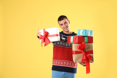 Photo of Happy man in Christmas sweater holding gift boxes on yellow background