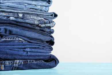 Photo of Stack of different jeans on blue wooden table. Space for text