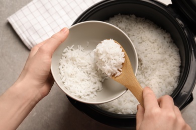 Photo of Woman putting rice into bowl from cooker in kitchen, top view