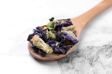 Photo of Spoon with dry organic blue Anchan on white marble table, closeup. Herbal tea