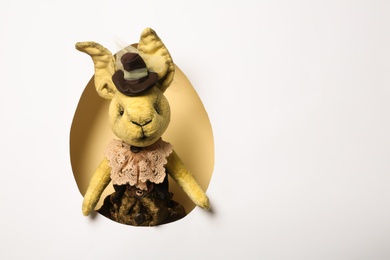 Photo of View of vintage Easter bunny toy on color background through egg shaped hole, top view. Space for text