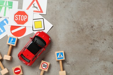Photo of Many different road signs and toy car on grey background, flat lay with space for text. Driving school