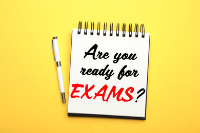 Image of Stylish notebook with phrase ARE YOU READY FOR EXAMS and pen on yellow background, top view