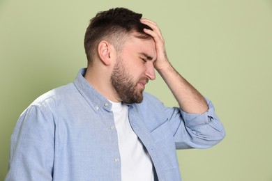 Man suffering from migraine on light green background