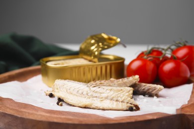 Photo of Delicious canned mackerel fillets and fresh tomatoes on wooden plate, closeup