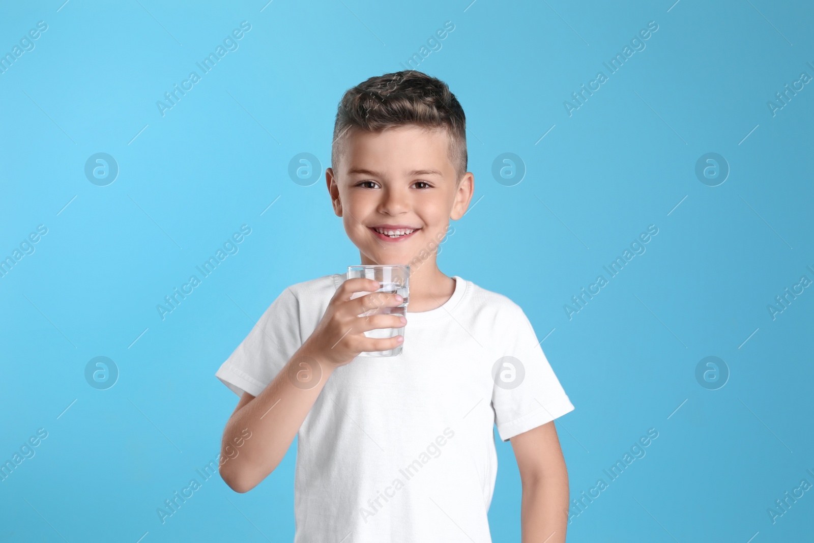 Photo of Cute little boy with glass of water on light blue background