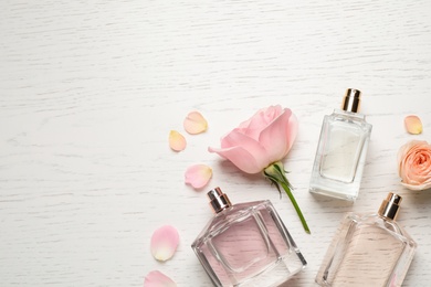 Photo of Flat lay composition with different perfume bottles and roses on white wooden background, space for text