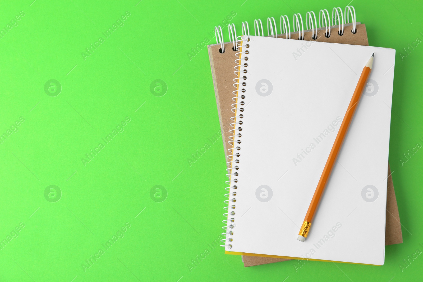 Photo of Notebooks with pencil on light green background, top view. Space for text