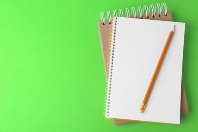 Notebooks with pencil on light green background, top view. Space for text