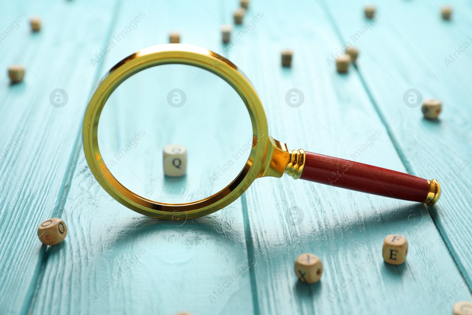 Photo of Magnifier glass and cube with letter Q on light blue wooden background, closeup. Find keywords concept