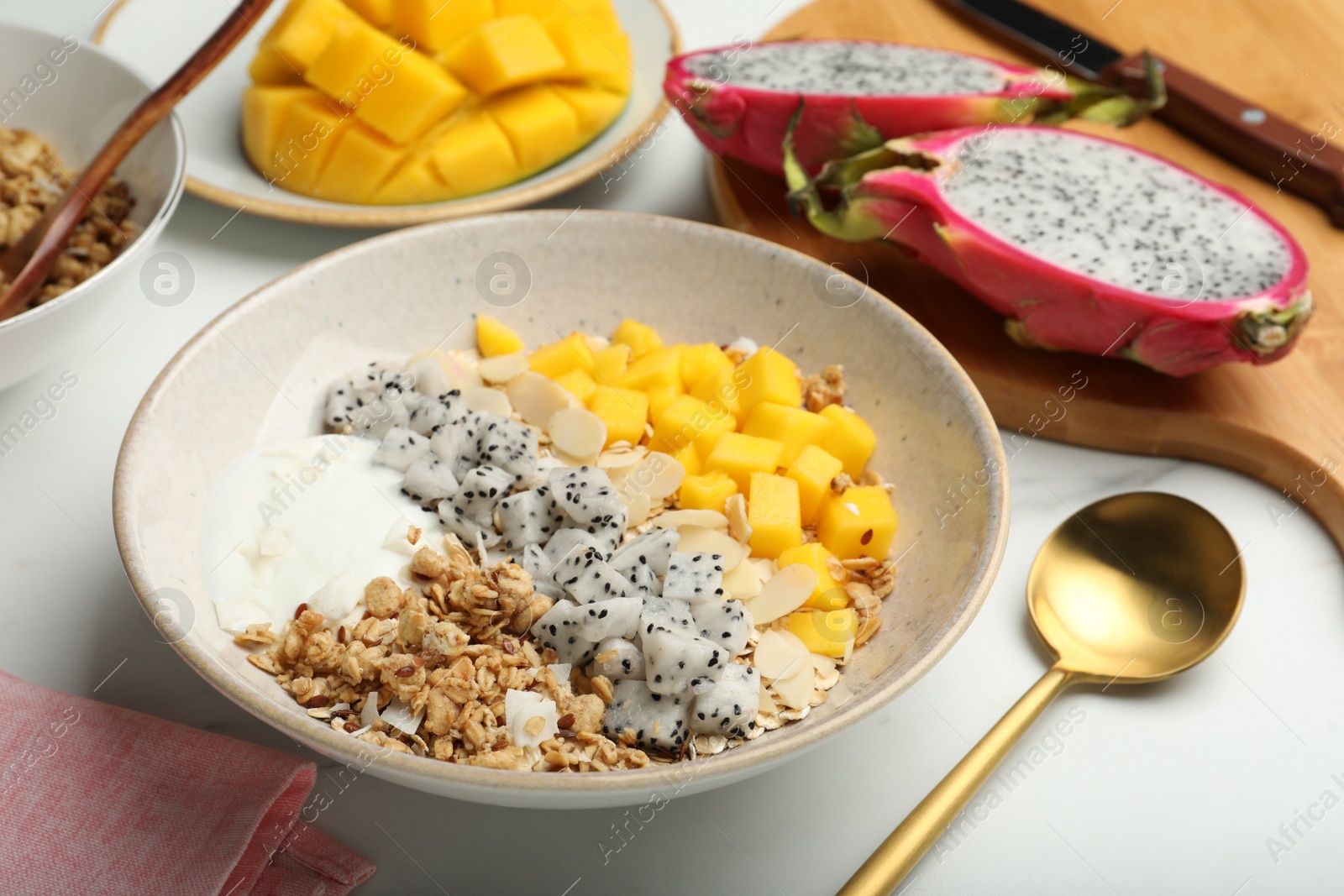 Photo of Bowl of granola with pitahaya, mango and yogurt on white marble table