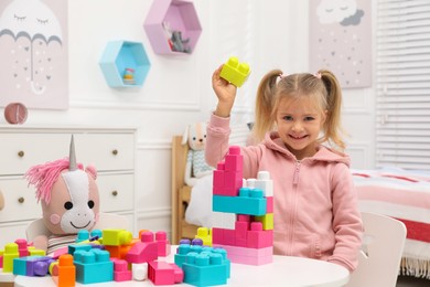Cute little girl playing with colorful building blocks at table in room, space for text