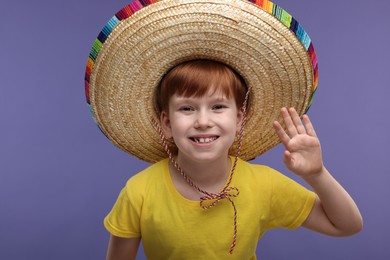 Cute boy in Mexican sombrero hat waving hello on violet background