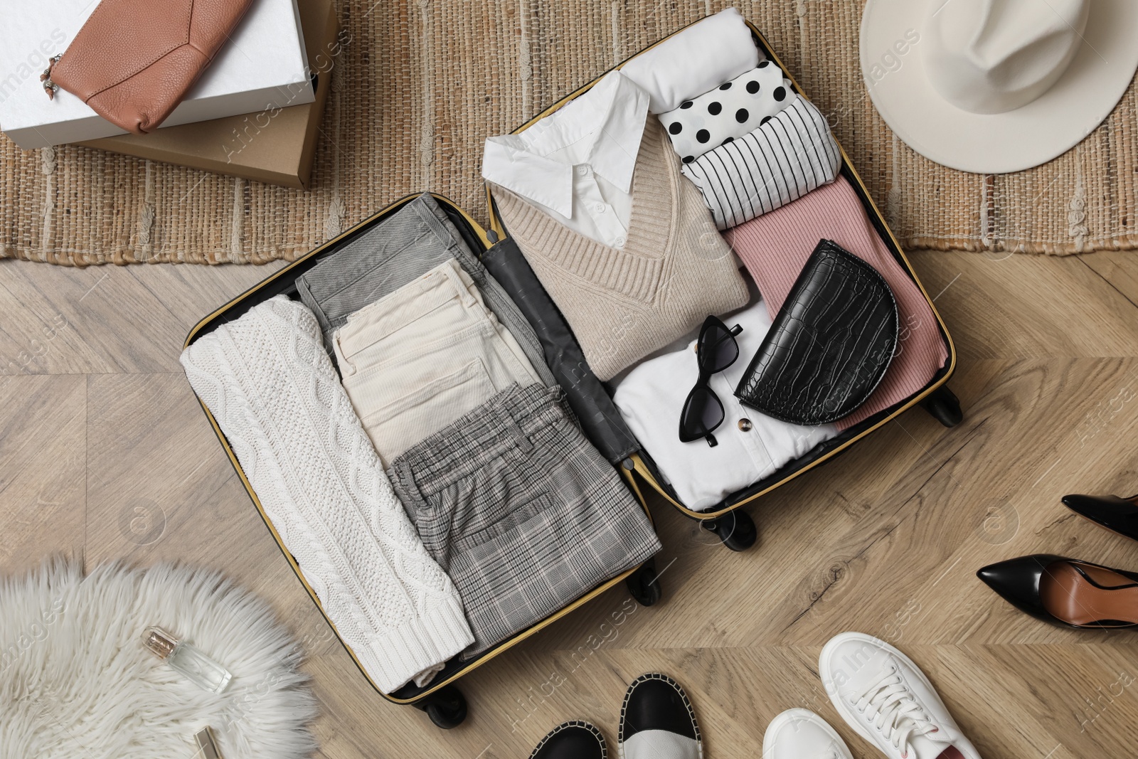 Photo of Open suitcase with folded clothes, accessories and shoes on floor, flat lay