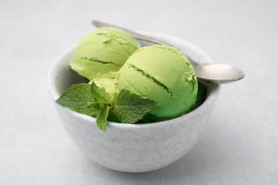 Tasty matcha ice cream and spoon in bowl on light grey table, closeup