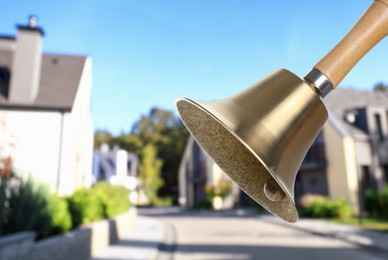 Image of Golden school bell with wooden handle and blurred view of street on sunny day
