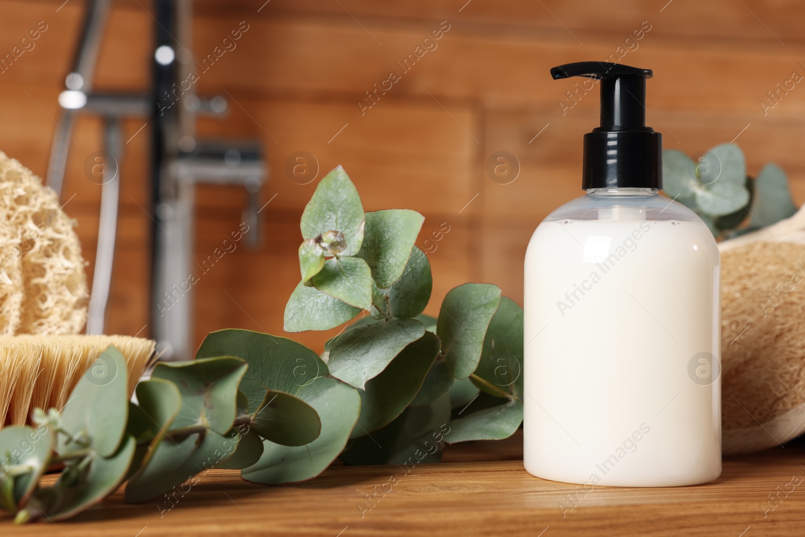 Photo of Dispenser of liquid soap and eucalyptus branch on wooden table