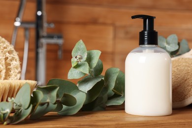 Dispenser of liquid soap and eucalyptus branch on wooden table