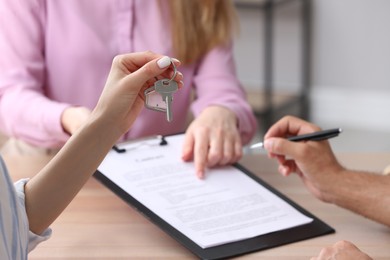 Photo of Woman holding new house key in real estate agent's office, closeup