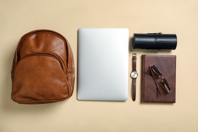Photo of Stylish urban backpack with different items on beige background, flat lay