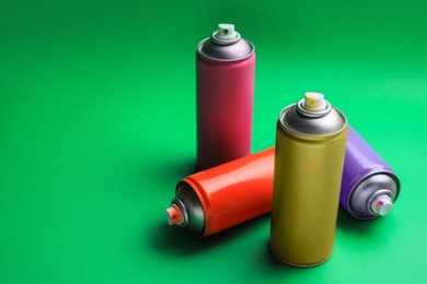 Cans of different graffiti spray paints on green background, space for text