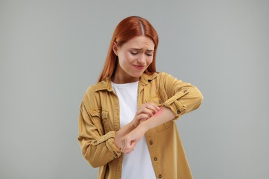 Photo of Suffering from allergy. Young woman scratching her arm on grey background