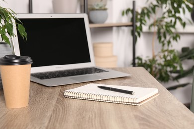 Paper cup, notebook and laptop on wooden table in room