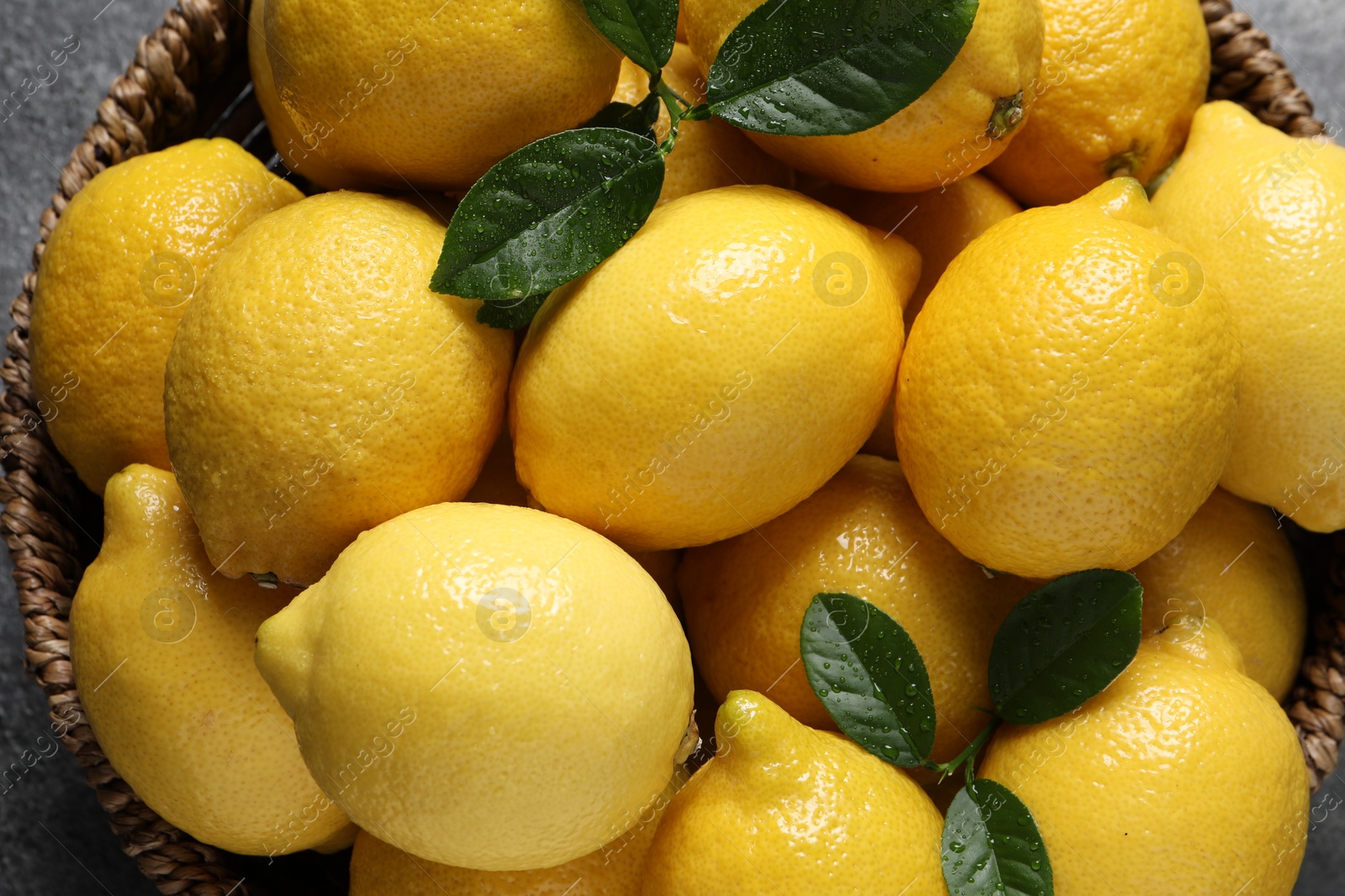 Photo of Fresh lemons in wicker basket on grey table, top view