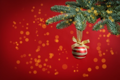 Beautiful Christmas ball hanging on fir tree branch against red background, bokeh effect. Space for text